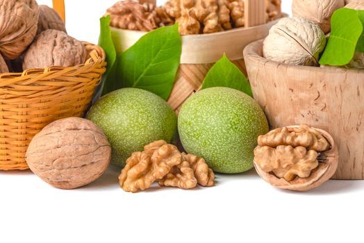 Walnut. Walnut fruits of different varieties lie in wooden saucers and baskets on a white isolated background. Nearby are green leaves and unripe walnut fruits