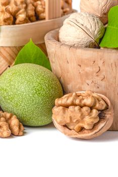 Walnut. Walnut fruits of different varieties lie in wooden saucers and baskets on a white isolated background. Nearby are green leaves and unripe walnut fruits