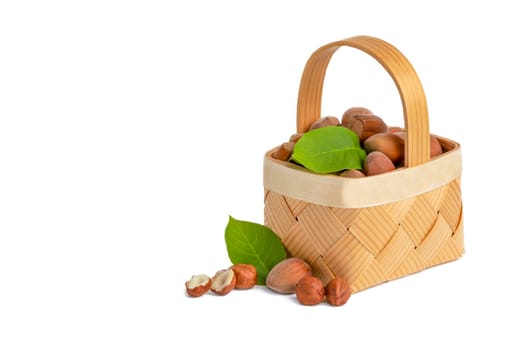 Hazelnut lies in a wooden basket on a white isolated background. Unpeeled hazelnuts in shell and green leaves.