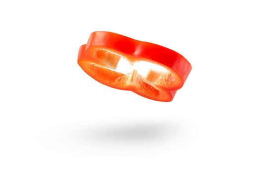 A slice of red paprika falls on a white backdrop. Red bell pepper flying in air on isolated white background.