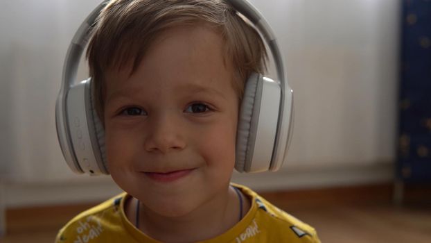 Close up handsome smiling boy listening to music headphones indoor. Children and technology. Love of music, children's dreams hobbies. Talented happy little child leasure. Childhood, musicality, hobby.