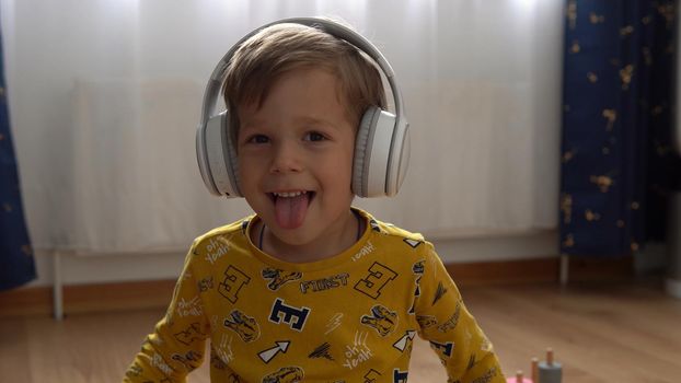 Close up handsome smiling boy listening to music headphones indoor. Children and technology. Love of music, children's dreams hobbies. Talented happy little child leasure. Childhood, musicality, hobby.