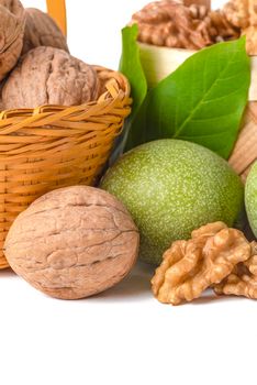 Walnut. Walnut fruits of different varieties lie in wooden saucers and baskets on a white isolated background. Nearby are green leaves and unripe walnut fruits