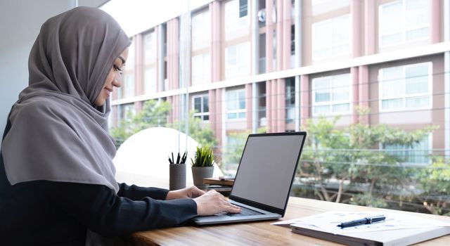 Happy arab woman freelancer chatting with clients on laptop, sitting at cafe, empty space.