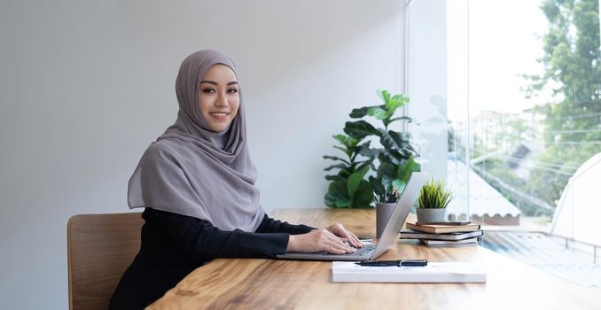 Happy arab woman freelancer chatting with clients on laptop, sitting at cafe, empty space.