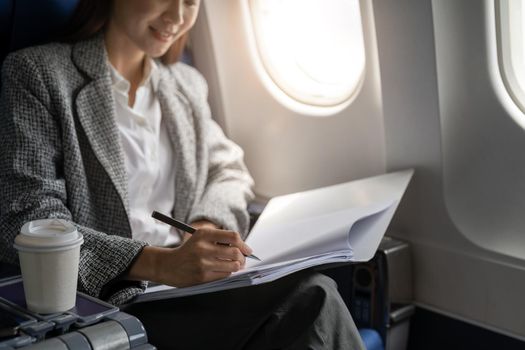 Close up hand of asian female entrepreneur working on paperwork finance report sitting near window in an airplane.