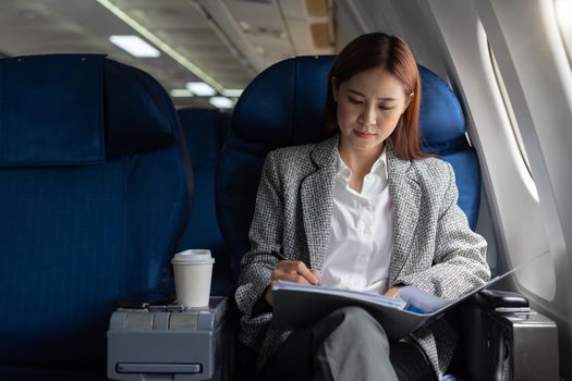 Asian female entrepreneur working on paperwork finance report sitting near window in an airplane.