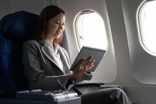 Travel and technology. Young asian woman in plane using digital tablet while sitting in airplane seat.