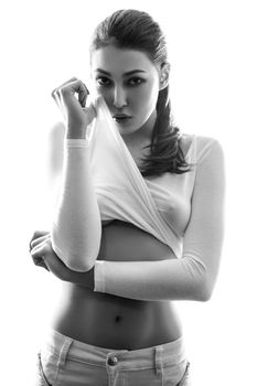 Beautiful young chinese european sexy fashion model posing in white t-shirt and undressing her white transparent shirt and looking at camera with passion. black and white photography, studio shot.