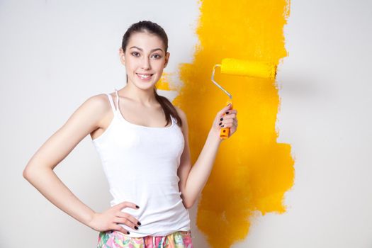 Beautiful young caucasian model in coloured shorts and white shirt and posing holding outrigger in her hands, painting the wall and looking at camera. Studio shot.