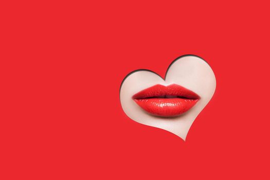 Beautiful woman red lips through red heart shape. indoor studio shot isolated on red background.