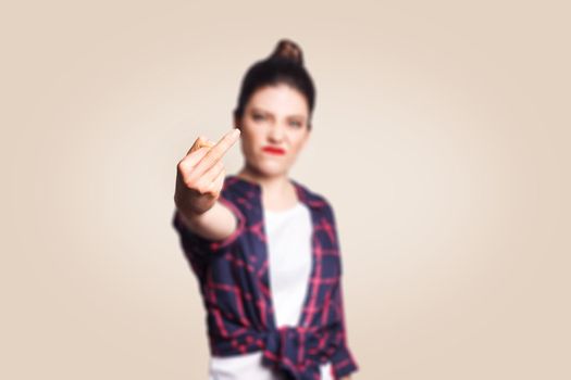 Middle finger sign. Unhappy angry young woman showing middle finger with unsatisfied face. studio shot on beige background. focus on fingers.