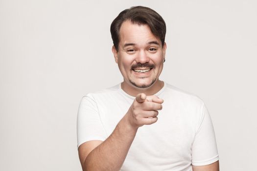 The happiness man, wearing white tshirt, having happiness looks, pointing finger at camera and toothy smiling. Isolated studio shot on gray background