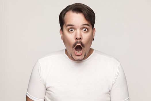 Isolated studio shot on gray background of happy successful adult man, feeling lucky, looking at camera, with open mouth.