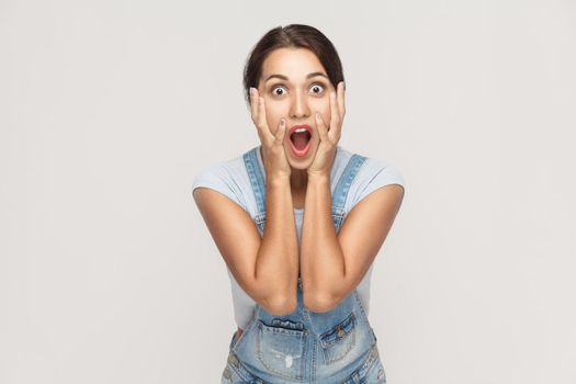 Human face expressions and emotions. Arab young adult woman holding arms on her cheeks and shocked. Isolated on gray background, studio shot