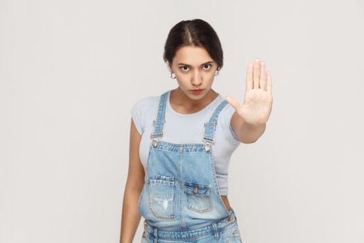 Isolated studio shot on gray background. Young annoyed woman with bad attitude making stop gesture with her palm outward, saying no, expressing denial or restriction.