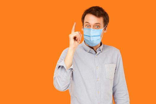 I have idea. Portrait of excited young worker man with surgical medical mask standing with surprised face and has a idea. indoor studio shot isolated on orange background.