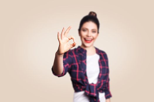 OK. Happy toothy smiley young woman showing OK sign with fingers. studio shot on beige background. focus on hand.