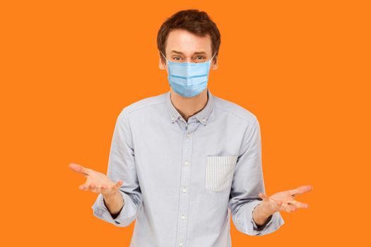 Portrait of sad stressed young worker man with surgical medical mask standing and looking at camera with sad face and asking. indoor studio shot isolated on orange background.