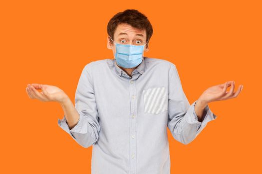 I dont know. Portrait of confused young worker man with surgical medical mask standing and looking at camera and asking. indoor studio shot isolated on orange background.
