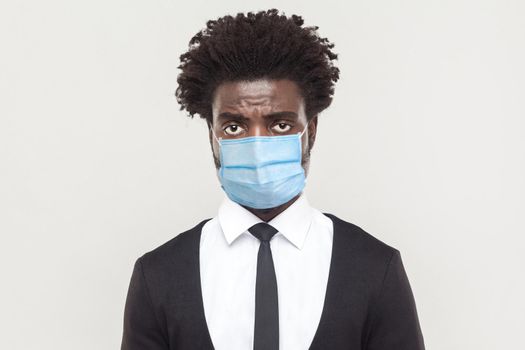 Portrait of sad alone young worker man wearing black suit with surgical medical mask standing and looking at camera with tired, alone or upset face. indoor studio shot isolated on gray background.