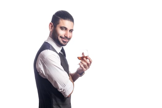 Handsome bearded businessman holding a glass of whiskey. holding glass and looking at camera with smile. studio shot, isolated on white background.