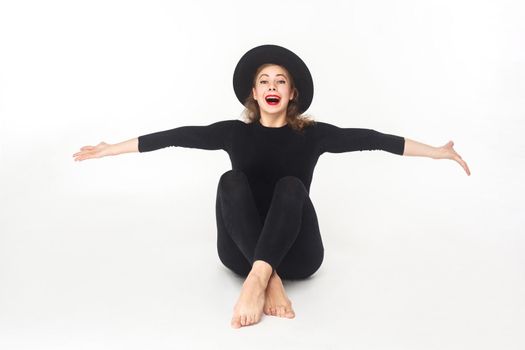 Happiness beautiful woman in hat, sitting on floor. Studio shot, isolated on white background