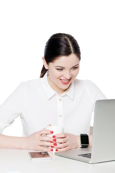 Portrait of happy attractive businesswoman in white shirt holding cup of drink, sitting and looking at laptop display, reading something and toothy smile. studio shot, isolated in white background.