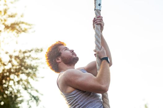 Climed higer and higher. Ginger sportsman doing exercise at rope. outdoor shot