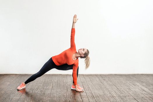 Slim blond woman in tight sportswear practicing yoga, standing in trikonasana triangle pose, training muscles for flexibility. Health care, sports activity and workout at home. indoor studio shot