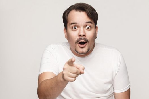 The adult man, opening mouths widely, having surprised shocked looks, pointing finger at camera. Isolated studio shot on gray background