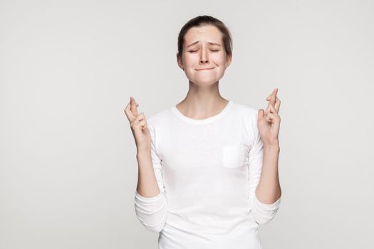 I wish some cool. Young beautiful girl closed eyes and crossed fingers. Studio shot,isolated on gray background