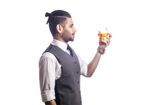 Handsome bearded businessman holding a glass of whiskey. side view. looking at glass and smiling, studio shot, isolated on white background.