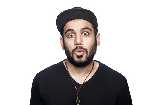 Portrait of young shocked surprised unhappy man with black t-shirt and cap looking at camera. studio shot, isolated on white background.