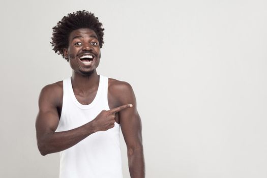 Man in white t-shirt showing finger at copy space. Studio shot. Gray background