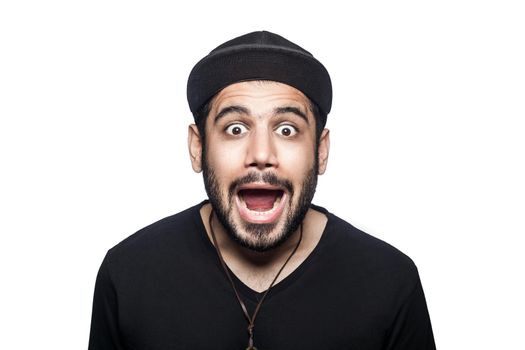 Portrait of young shocked surprised unhappy man with black t-shirt and cap looking at camera. studio shot, isolated on white background.