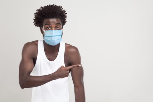 Look at this. Portrait of funny young man wearing white shirt with surgical medical mask standing and showing or sharing empty copy space on background. indoor studio shot isolated on gray background.