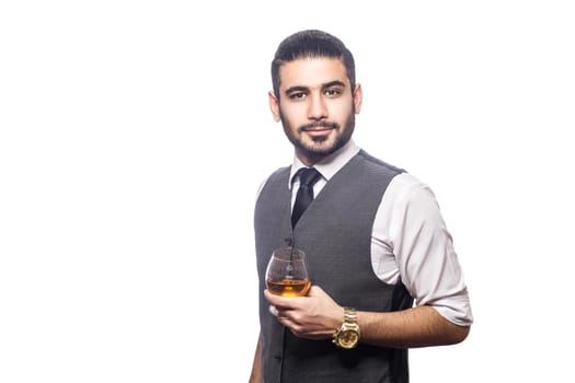 Handsome bearded businessman holding a glass of whiskey. holding glass, smiling and looking at camera. studio shot, isolated on white background.