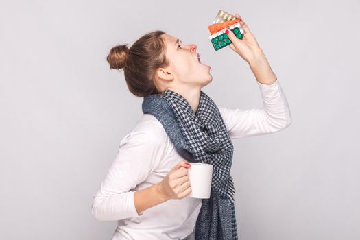 Sick young woman holding cup with tea, many pills and antibiotics. Studio shot, isolated on gray background