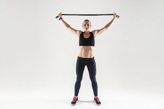 Trx equipment. Strong woman holding jumping rope near head and looking at camera. Studio shot, gray background