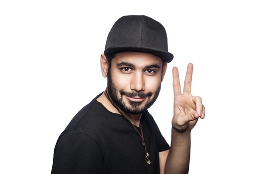 Portrait of young man with black t-shirt and cap looking at camera with victory sign. studio shot, isolated on white background.