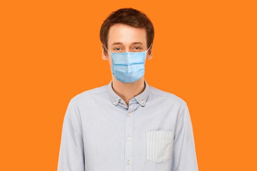 Portrait of young worker man with surgical medical mask standing and looking at camera smiling. health care and medicine concept. indoor studio shot isolated on orange background.
