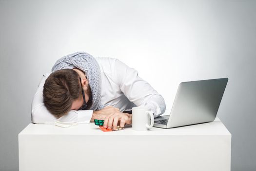 With temperature in the work station. Portrait of illness manager in white shirt are sitting in office is snoozing at his work place near laptop. Indoor, studio shot, gray background, isolated