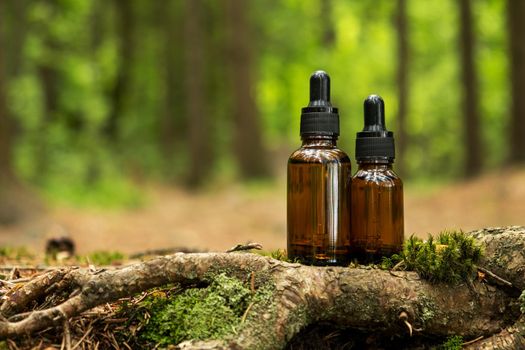 Two glass brown cosmetic containers with pipette are placed against backdrop of a natural forest. Concept of natural organic cosmetics, skin health. Selective focus..