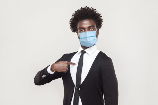 It's me. Portrait of proud young handsome worker man wearing black suit with surgical medical mask standing pointing himself and looking at camera haughty. indoor studio shot isolated on gray background.