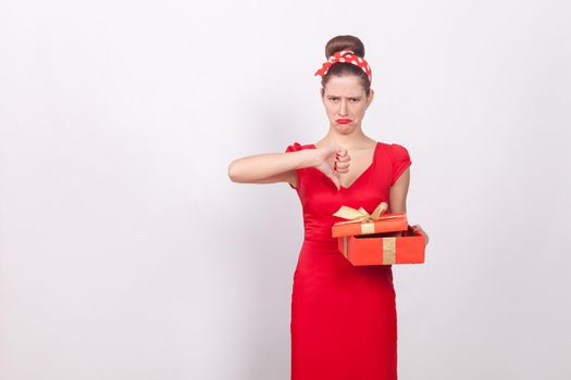 Dislike. Woman holding red box and demonstrate thumb down. Indoor, studio shot, isolated on gray background