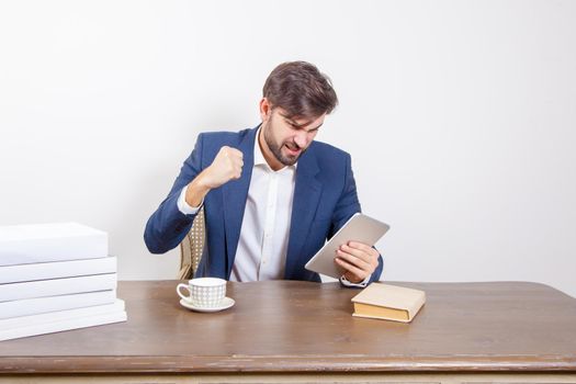 Technology, people and business concept - handsome man with beard and brown hair and blue suit and tablet pc computer and some books sitting in the office angry and unhappy. .Isolated on white background. .