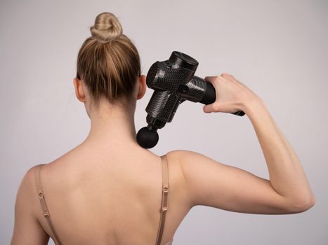 Caucasian woman giving herself a back massage with a gun