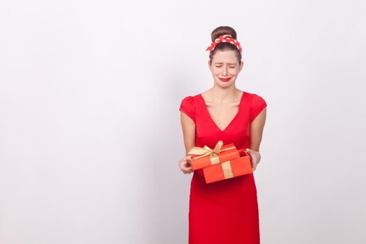 Disappointment. Woman holding red box and cry. Bad gift. Indoor, studio shot, isolated on gray background