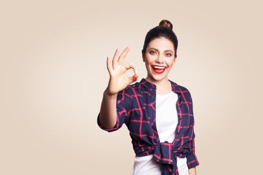 OK. Happy toothy smiley young woman showing OK sign with fingers. studio shot on beige background. focus on face.